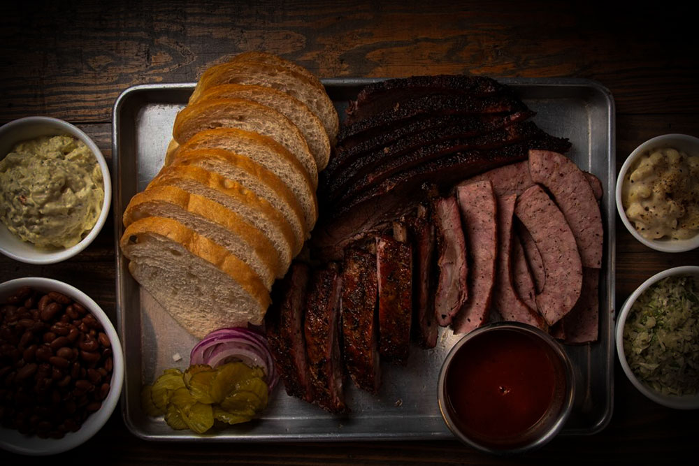 Perfect for a Guys Weekend or a 3 Day Itinerary in Burnet County, tray from Inmans is loaded with sliced white bread, brisket, ribs, sausage, pickles, onions, barbecue sauce, plus sides of baked beans, potato salad, coleslaw and macaroni and cheese.