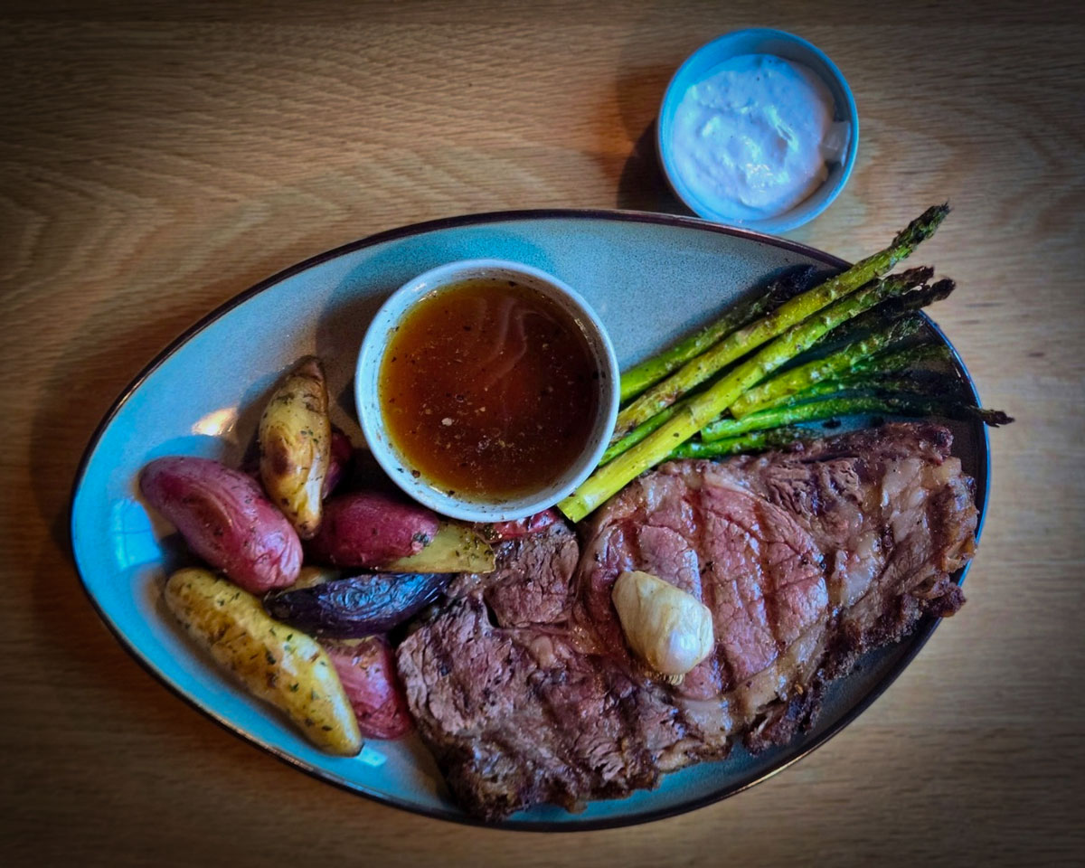 Perfect for a Guys Weekend in Burnet County, this plate features grilled steak with butter, roasted fingerling potatoes, grilled asparagus, au jus, and a creamy dipping sauce—all set on a rustic wooden table.